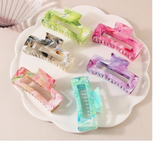 Set of six colorful marble pattern rectangular hair claws arranged on a ceramic plate