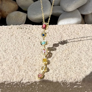 Detailed shot of gold necklace with colorful mixed-shape gemstones on natural stones