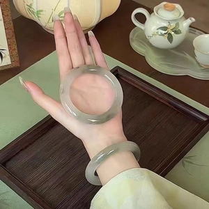Nahaufnahme von lichtgrünen Jade-Armreifen am Handgelenk mit Teekannen-Hintergrund im Detail