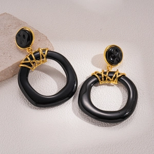 Close-up of black resin earrings with golden woven metal details on a stone surface