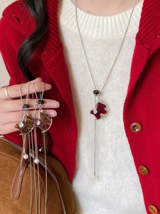Detail of a rocking horse necklace with red flocking and a white pearl drop on a sweater