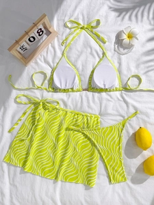 Three-piece neon green wave bikini set with halter top and skirt on white fabric
