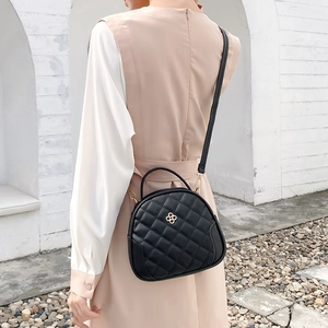 Quilted black crossbody bag with gold clover clasp shown in a stylish outdoor setting
