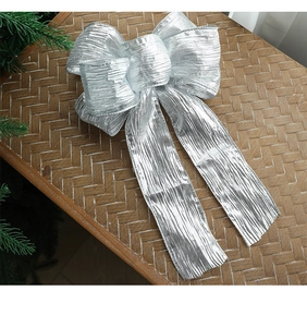 Macro detail of large silver textured fabric bow on woven surface with festive tree branch