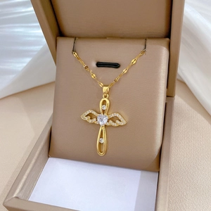Detail of gold angel wing cross pendant with heart gemstone in a beige jewelry box