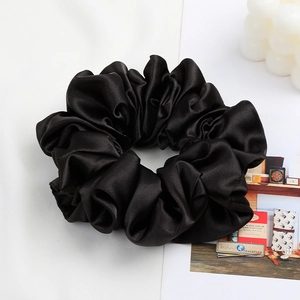Detail of a large black satin scrunchie with soft folds and elegant silk texture shine