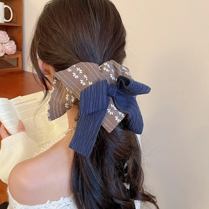 Detailansicht eines Vintage-Haargummis mit Blumenmuster und marineblauem Band am Pferdeschwanz
