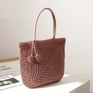 Handmade straw tote bag with pink pom pom tassel on a white minimalist display stand