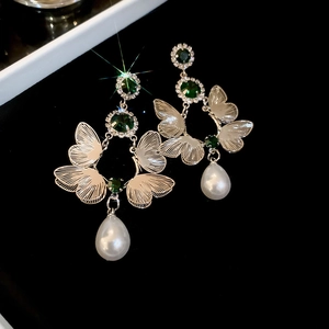 Detail of vintage emerald earrings with metallic wings and teardrop pearl pendants