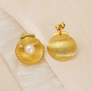 Macro view of shell-shaped gold earrings with white pearl inlay and metal texture