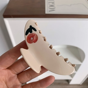 Close-up of beige hair claw clip with swallow patterns and rhinestones on a table