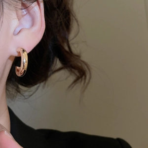 Side view detail of a polished gold C-shape hoop earring worn on a model with soft lighting
