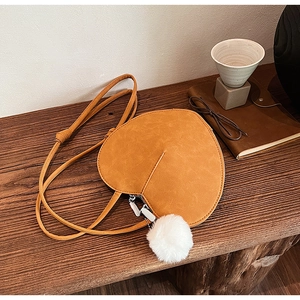 Detail einer ingwerfarbenen herzförmigen Wildledertasche mit weißem flauschigem Anhänger