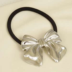 Detail shot of a black elastic hair tie with a silver metal bow on beige fabric