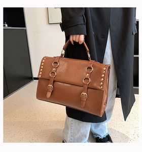 Detail of vintage brown shoulder bag showing metal rivets and buckle straps on leather texture