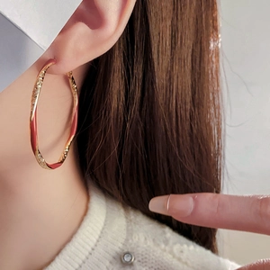 Close-up of a model wearing a gold and red enamel twisted hoop earring with hammered texture