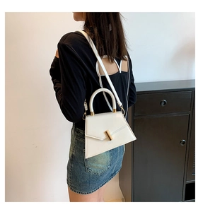 Close-up of white geometric handbag featuring a gold cylindrical metal clasp and handle