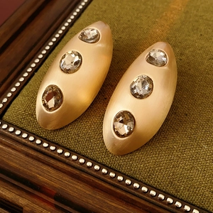 Detailed view of matte gold oval earrings with three sparkling inlaid crystals on fabric
