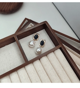 Dettaglio macro di orecchini con perle barocche e strass in un portagioie di legno