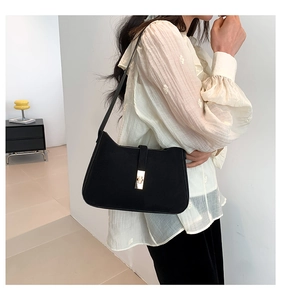 Detail of black suede shoulder bag featuring a premium gold metallic clasp closure