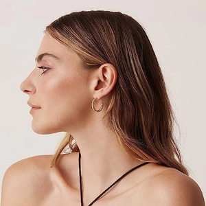 Close-up of elegant 18k gold plated twisted hoop earrings worn by a model in soft light
