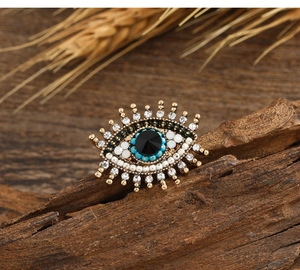 Detailed view of evil eye brooch with blue beads and crystals on rustic wood background
