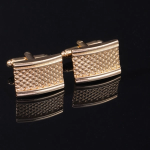Macro view of gold square cufflinks with engraved checkered pattern on reflective black base