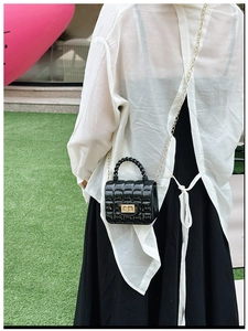 Outdoor back view of a black quilted PVC mini bag with gold chain and handle