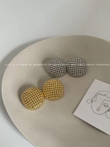 Macro detail of gold and silver hollowed beaded stud earrings on ceramic plate