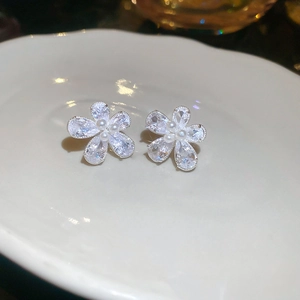 Macro view of silver flower stud earrings with sparkling zircons and delicate mini pearls