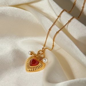 Macro detail of 18k gold heart pendant with red agate stone and pearls on silk