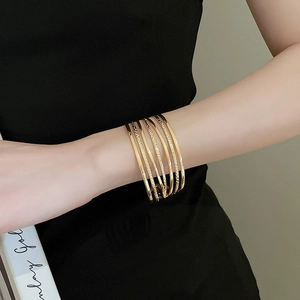 Detail of layered gold wide cuff bracelet with textured and smooth metallic finish