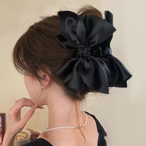 Detail of a large black satin bow claw clip styled in a woman's hair for an elegant look