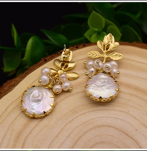 Detailed macro view of baroque pearl earrings with golden leaf design on wood background