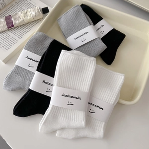 Set of three ribbed cotton mid-calf socks in white, gray, and black on a minimalist tray