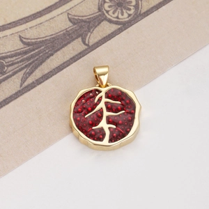 Détail d'un pendentif pépin de grenade rouge avec monture dorée et boucle de suspension