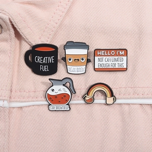 Détail de cinq pin's émaillés sur le thème du café fixés sur un tissu en jean rose