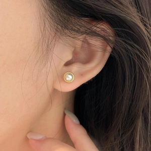 Close-up of elegant pearl stud earring with golden beaded edge worn on ear