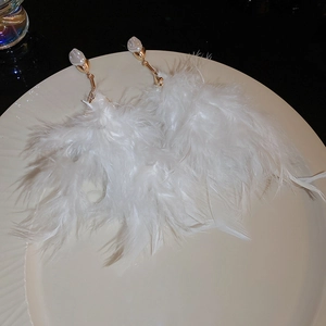 Detail of long white feather tassel earrings with gold hardware and pearls on a dish