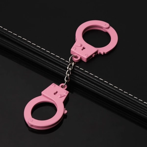 Detail of pink metal handcuffs with matte finish on black leather reflective surface