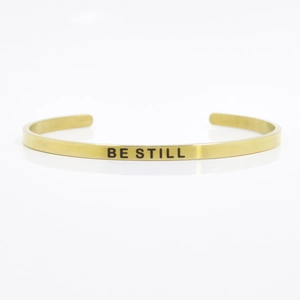 Detailed macro view of 4mm gold stainless steel cuff featuring BE STILL engraved text