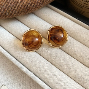 Close-up of amber resin round stud earrings with gold trim on beige velvet stand