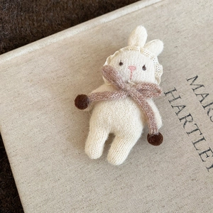 Detail of a handmade knitted beige bunny brooch with lace collar and brown bow detail