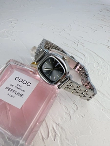 Detail of silver square dial watch on pink perfume bottle with metallic chain strap