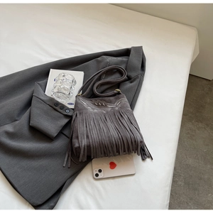 Close-up of a gray suede crossbody bag featuring long fringes and white embroidery details
