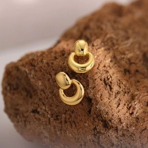 Detailed close-up of golden teardrop earring placed on a natural brown rock surface