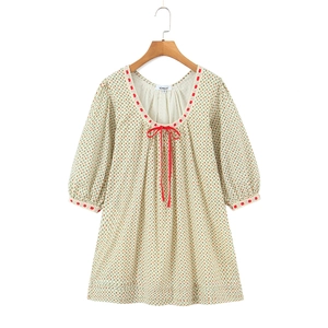 Detail van rood kant en strik op een beige gebloemde jurk met pofmouwen