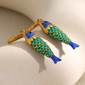 Detailed view of fish-shaped gold earrings with blue and green enamel on a matte surface