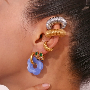 Macro shot of 18K gold earrings set with blue acrylic flower charm and stone ear cuffs