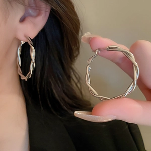 Detailed view of silver twisted hoop earring on ear showcasing minimalist metal texture